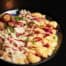 A bowl filled with mac and cheese shells, tater tots, roasted turkey drizzled with turkey gravy, cranberry and green onions.