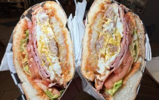 Bagel with two fried eggs, melted cheese, chipotle mayo, ham, breakfast sausage, fried hashbrown patty, hot sauce, lettuce and tomato