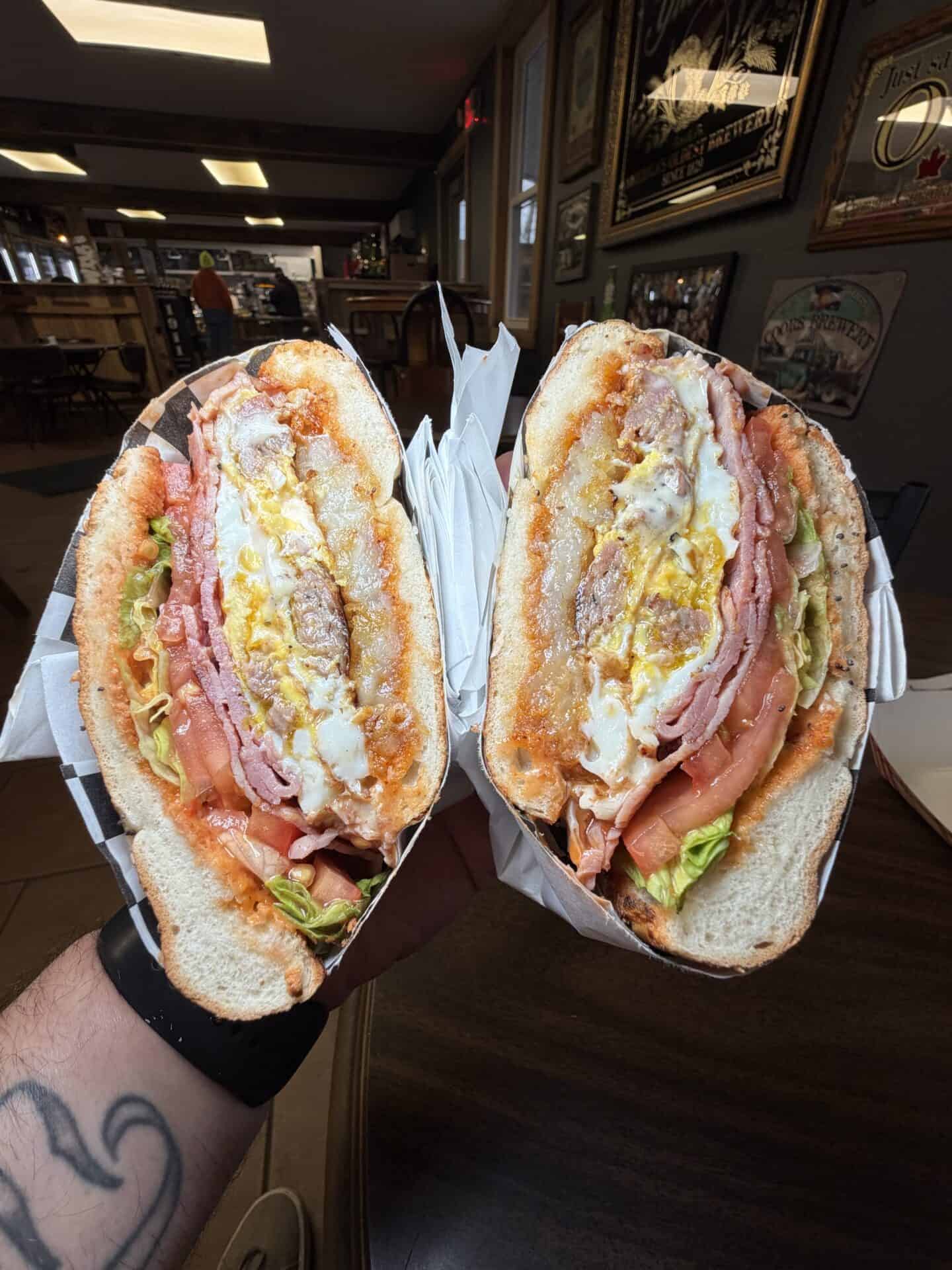 Bagel with two fried eggs, melted cheese, chipotle mayo, ham, breakfast sausage, fried hashbrown patty, hot sauce, lettuce and tomato
