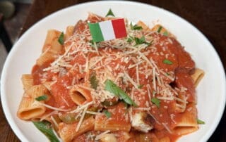 Plate of chicken riggies in a red sauce, with parmesan cheese and an Italian flag on top of the pile of rigatoni pasta.