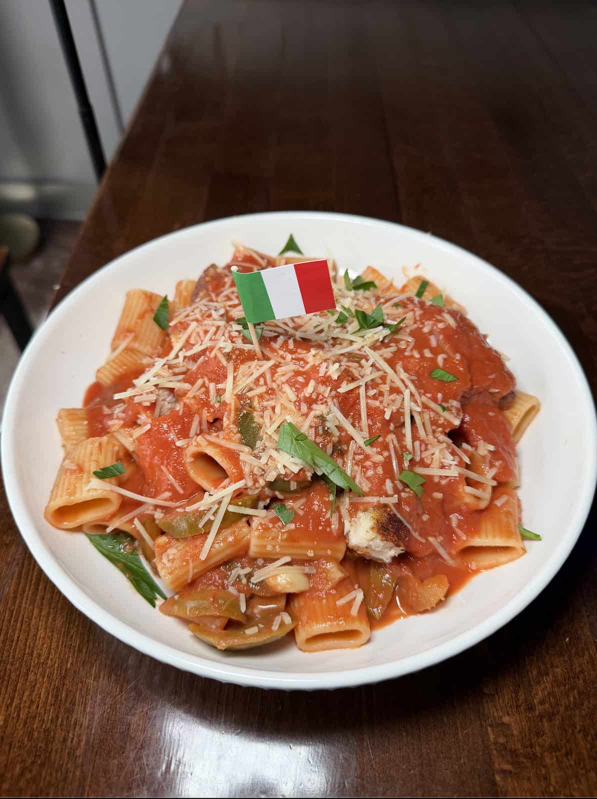 Plate of chicken riggies in a red sauce, with parmesan cheese and an Italian flag on top of the pile of rigatoni pasta.