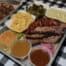 A tray of BBQ food. Brisket, sausage, cornbread, Mac and cheese, collard greens and sauces from Rev BBQ in Rochester, NY.